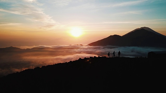 一群朋友跑上山，站在巴圖爾活火山山頂的云層之上，在巴厘島的日出空中拍攝4K視頻素材
