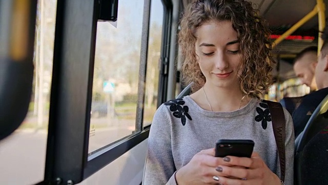 一位年轻女士在公交车上使用智能手机视频购买
