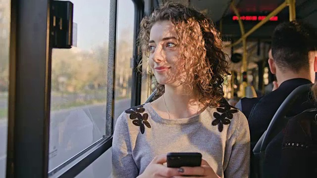 一位年轻女士在公交车上使用智能手机视频购买