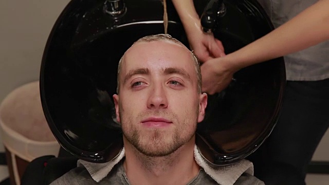 一位妇女在理发店里用洗发水和护发素给留胡子的男子洗头。洗掉洗头水视频下载