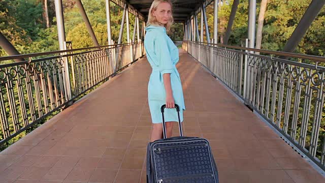 美丽的女人带着行李离开酒店，走在度假城市的街道上视频下载