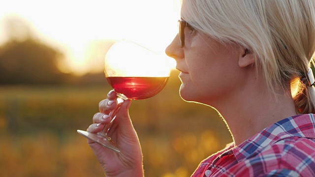 一个女人在品尝红酒。日落时分，拿着酒杯站在葡萄园旁边视频素材