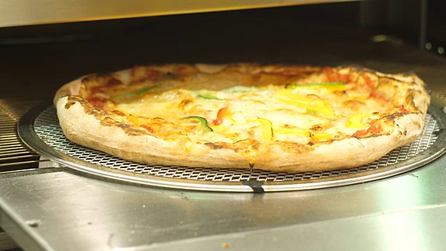 披萨从自动烤箱里出来，奶酪融化了，厨师拿走了它。视频素材
