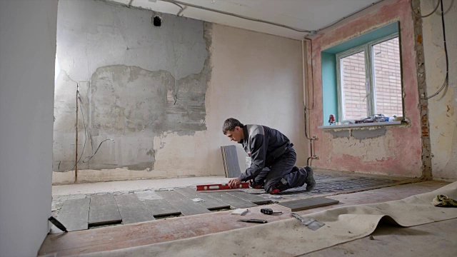 在住宅中工作的建筑工人将瓷砖铺在地板上，并用水平仪检查地板的坡度和平整度视频下载