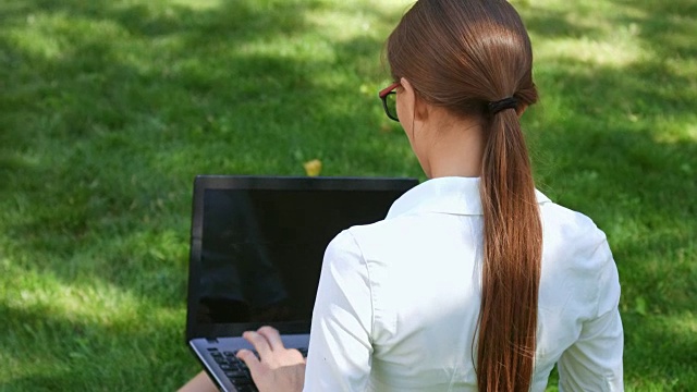 女商人在公园里工作，坐在绿色的草地上用笔记本电脑视频素材