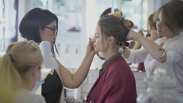 三位专家在美容院为年轻女士打造时尚形象视频下载