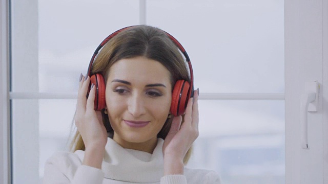 漂亮的女孩戴着耳机听音乐，在窗前跳舞视频素材