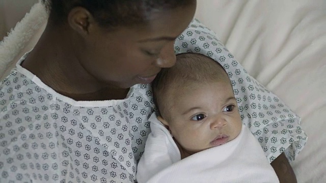 年轻的非裔美国母亲抱着她的混血女婴，穿着病号服视频下载