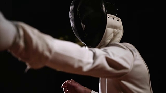 一个男人的特写镜头戴着一个头盔的击剑格斗与一个对手在一个黑暗的背景视频素材