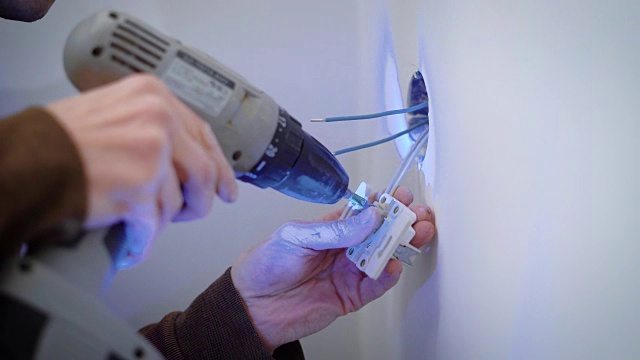 在室内维修过程中，电线工人使用螺丝将电线连接到电源插座上视频下载