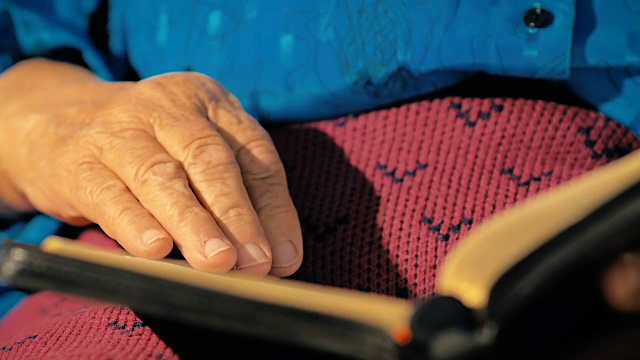 慢镜头:八十岁的女人慢慢翻动着金页书。视频素材