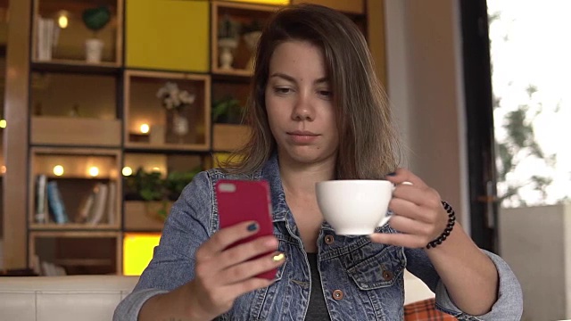 年轻女子拿着手机坐着喝咖啡视频素材