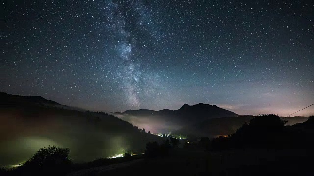 在繁星点点的夜空中，银河的星星在迷雾笼罩的山谷上方移动视频素材