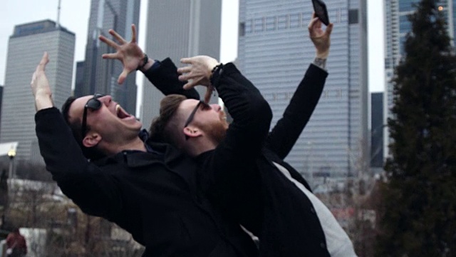 两个朋友在芝加哥公园用智能手机自拍，一边大笑一边俯瞰城市天际线。视频下载
