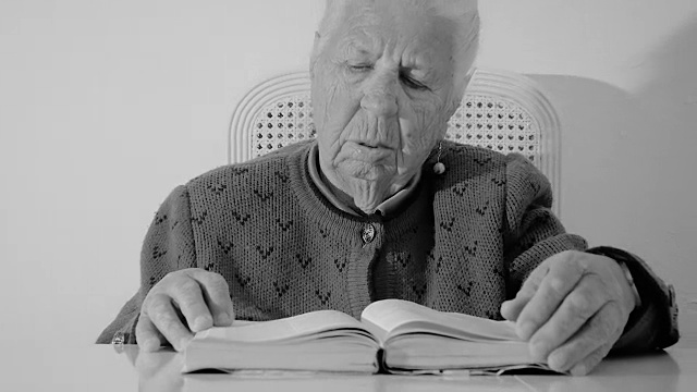 特写一位83岁的老妇人坐在家里的桌子旁，慢慢翻动书页。视频素材