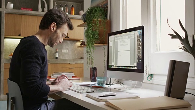 微笑的男人使用电脑在家庭办公室的办公桌视频素材