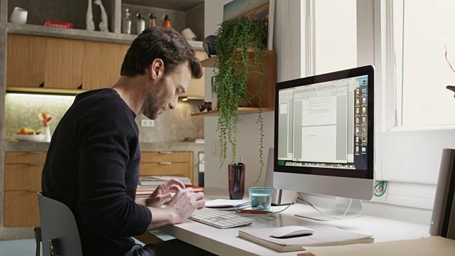微笑的男人使用电脑在家庭办公室的办公桌视频素材