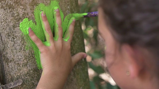 快乐的小女孩在夏令营的树上留下彩色的手印，外面的艺术，孩子们在户外的公园在树下玩耍的慢镜头视频下载