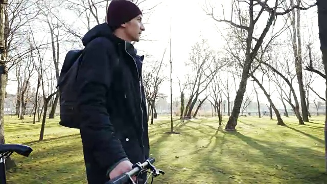 一个年轻人推着他的自行车在一个阳光灿烂的日子。视频下载