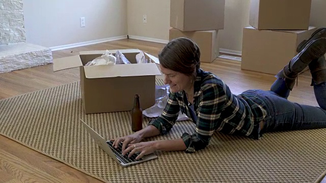 一个女人躺在客厅的地毯上，看着笔记本电脑。视频下载