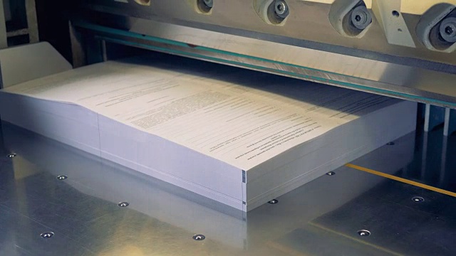一个工人把纸放入切纸工业机器的特写镜头。4 k。视频下载
