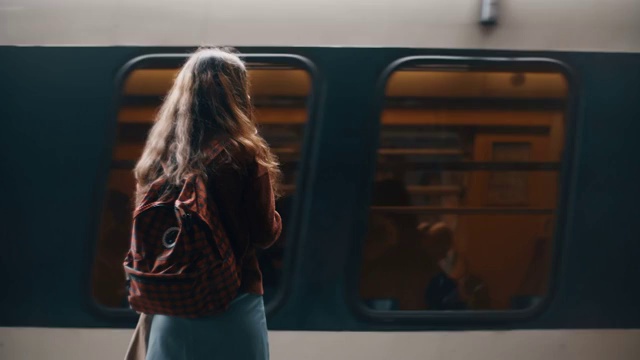 后视图的年轻女学生与背包站在地铁附近的快速乘坐火车，等待旅行视频购买
