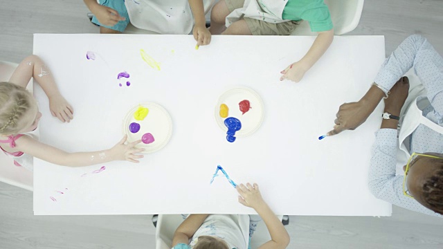 一群孩子在干净的白色桌子上画手指画视频下载