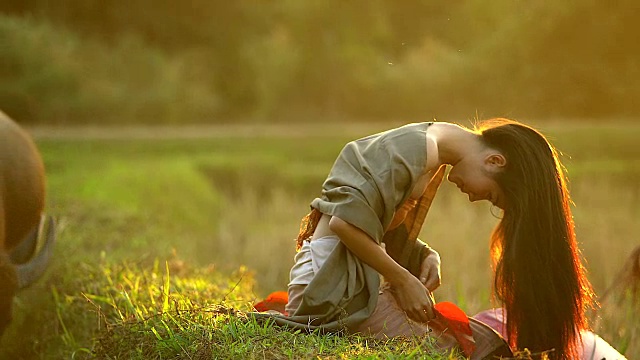 美丽的亚洲女人的肖像坐在傍晚与温暖的照明日落的田野。视频下载