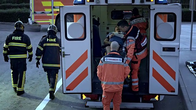 消防员和医护人员将一名受伤的骑自行车男子的担架推到救护车上视频下载