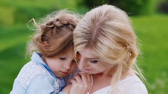 穿着漂亮的母亲和她的女儿轻轻地拥抱在绿色的树叶的背景视频素材