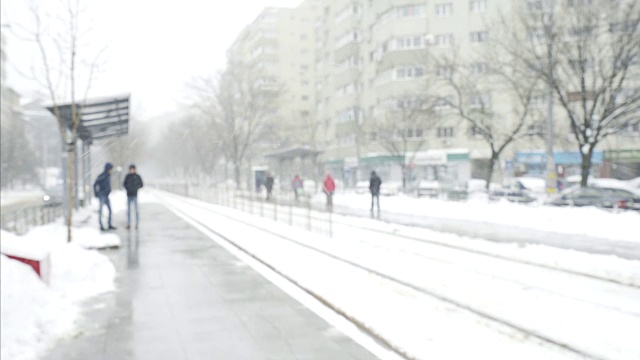 有轨电车车站偶然的人，寒冷的冬天，下雪的城市视频下载