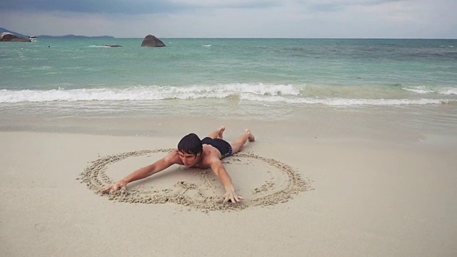 年轻人在海边潮湿的沙滩上画了一个心形符号。缓慢的运动。1920 x1080视频下载