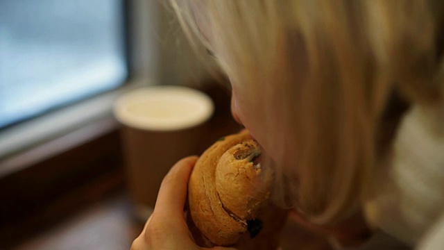 一位年轻女子正坐在咖啡厅里享用法式早餐，喝着咖啡，吃着牛角面包视频素材