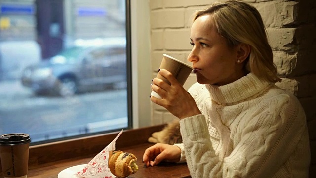 一位年轻女子正坐在咖啡厅里享用法式早餐，喝着咖啡，吃着牛角面包视频素材