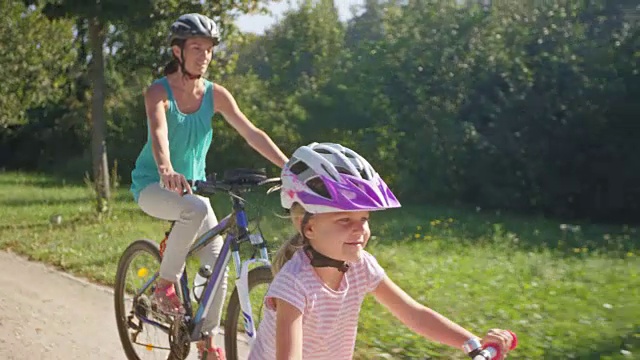 妈妈和小女儿在阳光明媚的公园里骑自行车视频素材