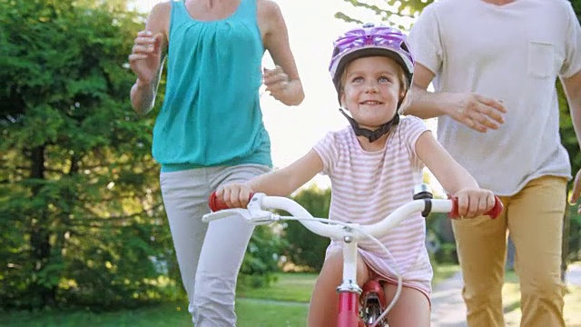 父母们在第一次骑自行车的女孩旁边跑步并鼓掌视频素材