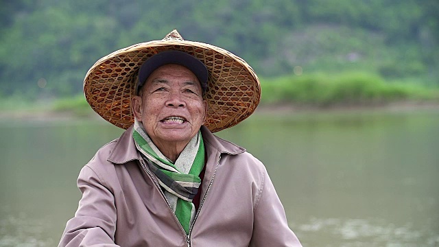 肖像快乐的资深亚洲渔民与一个笑脸坐在河边。视频下载
