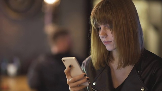 年轻漂亮的红发女子坐在咖啡馆或酒吧里用智能手机视频素材