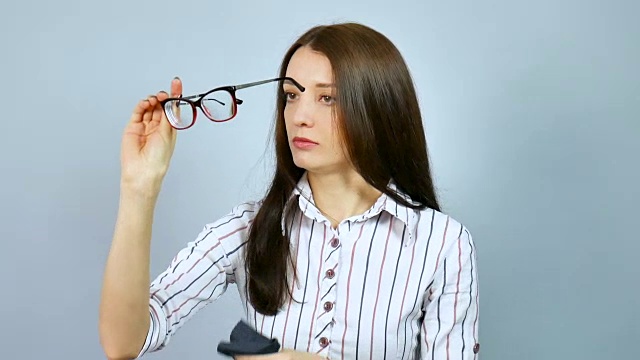 严肃的商业女人在白色衬衫与红蓝条纹擦拭她的光学眼镜和之后戴上他们对着她的脸和看镜头。视频下载