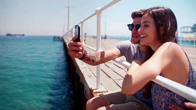一对快乐的年轻潮人情侣在木栈桥上用智能手机视频聊天视频下载