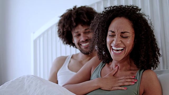 中年人深肤色的爱夫妇幸福地在家里一起在白色的床上度过一个周末，一起玩得很开心。视频素材