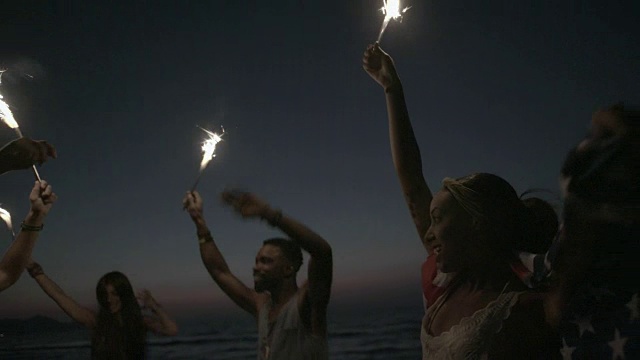 多民族的朋友在海滩上用烟花和美国国旗聚会视频下载