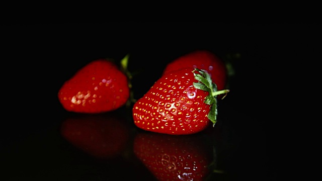 三颗草莓美丽地躺在黑色的桌子上，在一缕光线的背景下。高清视频下载