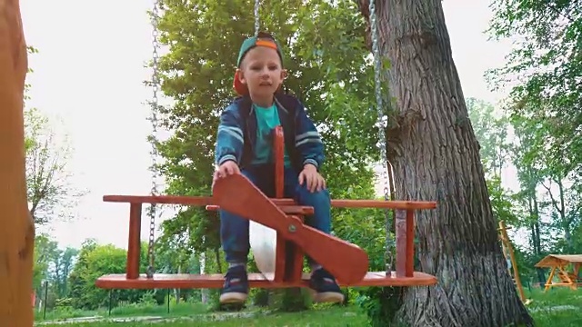 阳光下，一个快乐的小男孩在公园里的飞机木制秋千上。一个孩子在荡秋千玩得很开心视频素材