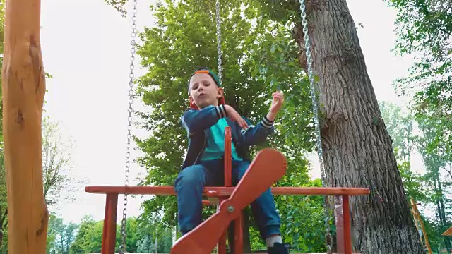 阳光下，一个快乐的小男孩在公园里的飞机木制秋千上。一个孩子在荡秋千玩得很开心视频素材