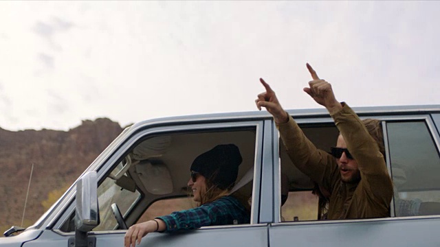 一群兴奋的朋友在摩押公路旅行途中向车窗外挥手欢呼。视频下载
