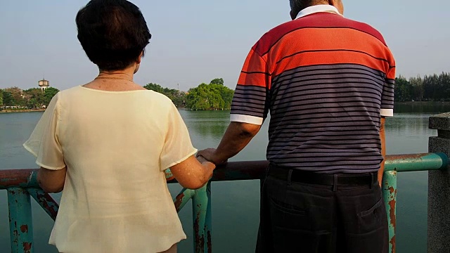 幸福浪漫的资深亚洲情侣站在湖边的桥上。丈夫和妻子站在一起。老年夫妻互相照顾的概念视频素材