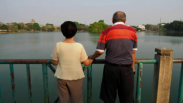 幸福浪漫的资深亚洲情侣站在湖边的桥上。丈夫和妻子站在一起。老年夫妻互相照顾的概念视频素材