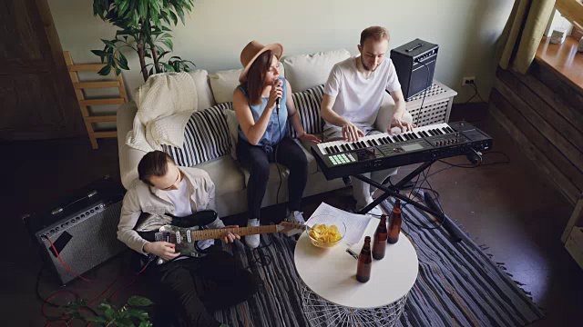 高视角的乐队排练在家庭工作室。情绪活跃的年轻人正在弹奏乐器、键盘、吉他和唱歌。视频下载