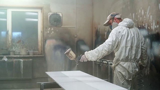 戴着防护面具和工作服的成熟男子在小制造厂为家具的细节上色视频素材